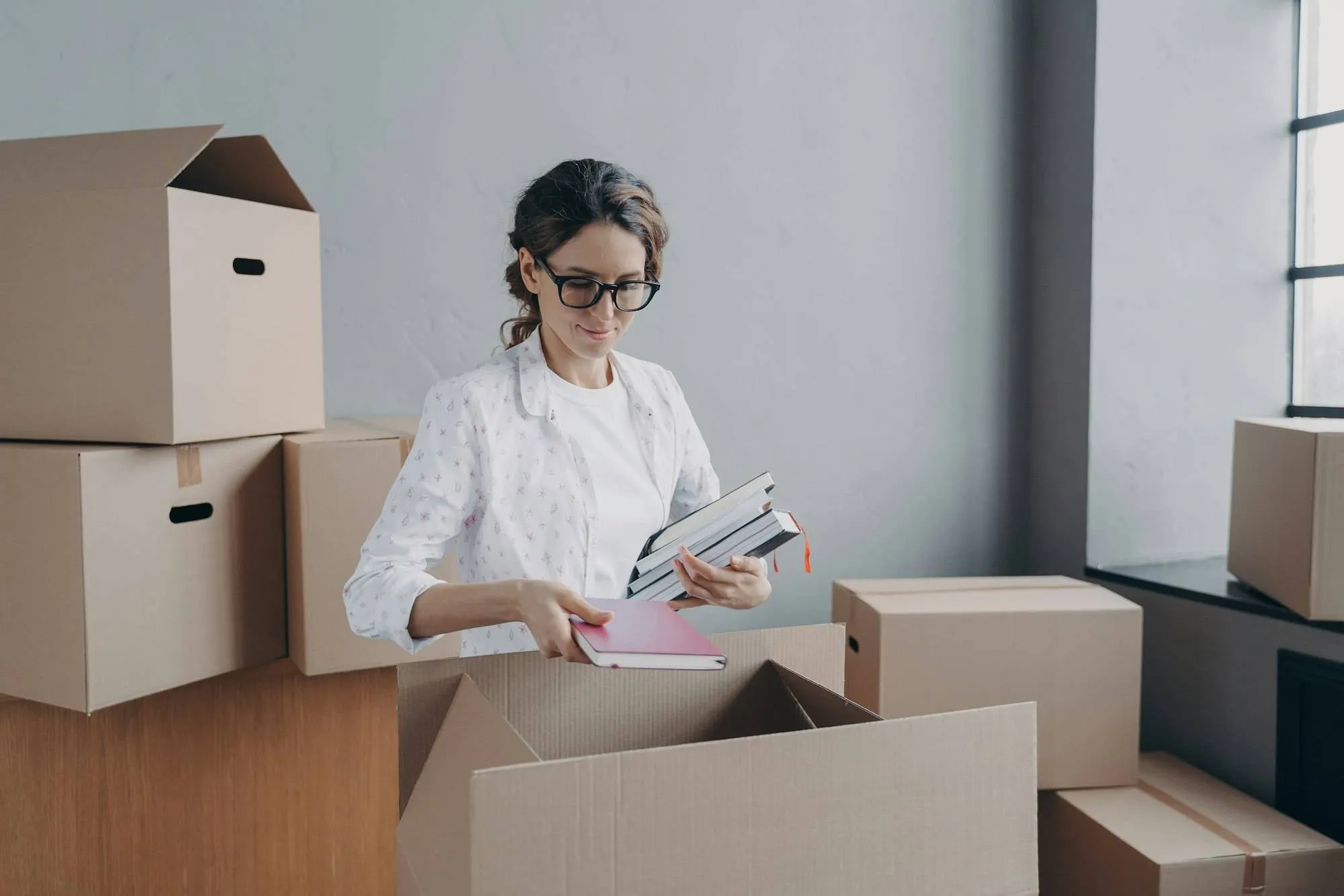 Femme triant des documents et livres près de cartons, contexte déménagement entreprise, check list déménagement entreprise etude.